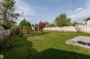 Expansive green lawn featuring a concrete patio, wood privacy fencing, mature trees, and two storage sheds - 4620 37A Avenue, Edmonton, AB  - Outdoor With Backyard 