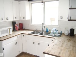 White cabinetry with contemporary black hardware, wood-finish countertops, and a white subway tile backsplash - 