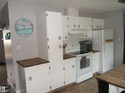 Kitchen featuring white cabinetry with dark hardware, wood-finish countertops, and a white subway tile backsplash - 