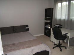 Carpeted interior room featuring neutral wall tones, a large window with sheer drapes, and a built-in shelving unit - 