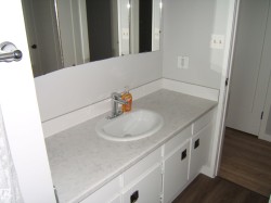 Bathroom vanity with a white oval sink, chrome single-handle faucet, and white countertop with integrated backsplash - 