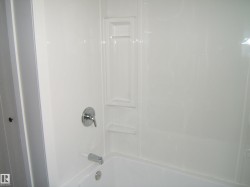 Crisp white tub and shower surround featuring integrated shelving, chrome fixtures, and a single-handle faucet - 