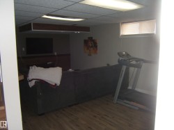 Recreational space featuring wood-finish flooring, a drop ceiling with integrated lighting, and a built-in entertainment center with wainscoting - 