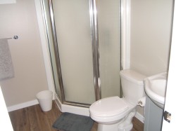 Bathroom featuring a corner shower with frosted glass enclosure, white toilet, and a white pedestal sink - 