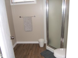 Compact bathroom featuring a stand-up shower with frosted glass enclosure, wood-finish flooring, and a small window with blinds - 