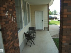 Covered concrete entryway featuring brick columns, white house numbers, and a paneled entry door - 