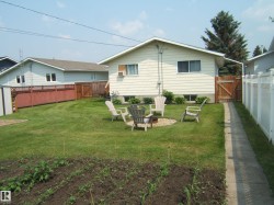 Spacious rear yard featuring an established garden bed, a manicured lawn, and a stone fire pit area - 