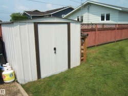 White metal storage shed with a brown trim and a single entry door - 