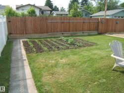 Expansive lawn area featuring a garden bed, a concrete pathway, and a wood fence - 