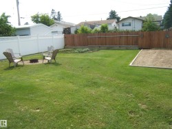 Expansive grassy yard featuring a white vinyl privacy fence, a wood privacy fence, and a designated garden bed - 