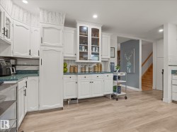 Kitchen featuring white cabinetry with dark hardware, a glass-front display cabinet, and light wood-finish flooring - 