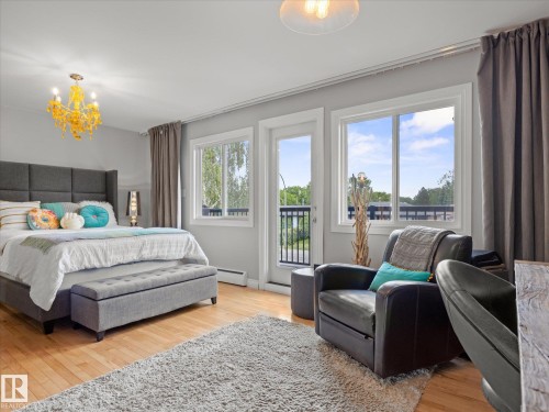 Spacious bedroom featuring light wood-finish flooring, a yellow chandelier, and light gray walls - 8822 161 Street, Edmonton, AB 