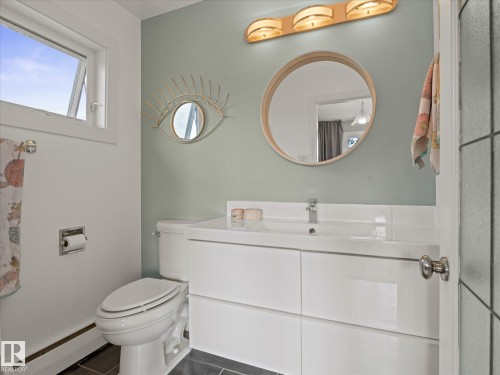 Bathroom featuring a modern white floating vanity with an integrated sink and chrome faucet, a circular mirror, and a three-light vanity fixture - 8822 161 Street, Edmonton, AB 