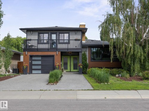 Contemporary two-story exterior featuring a balcony, wood-look siding, a modern garage door with frosted panels, and a vibrant green double entry door - 8822 161 Street, Edmonton, AB 