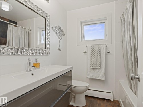 Bathroom featuring a floating vanity with an integrated sink, a rectangular mirror with a textured frame, and wood-finish flooring - 8822 161 Street, Edmonton, AB 