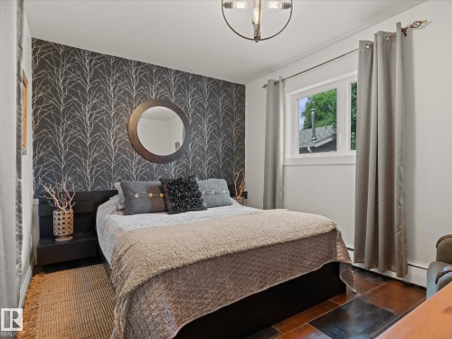 Bedroom featuring a striking accent wall with a tree branch pattern, a circular mounted mirror, and a modern ceiling light fixture - 8822 161 Street, Edmonton, AB 