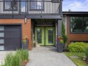 Modern exterior featuring wood-finish siding, a vibrant lime green double entry door, an integrated garage with frosted panel inserts, a second-story balcony with dark railing, and a concrete walkway - 8822 161 Street, Edmonton, AB 