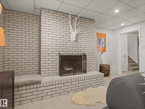 White painted brick fireplace with a black metal screen, integrated hearth seating, and a drop ceiling with recessed lighting - 8822 161 Street, Edmonton, AB 