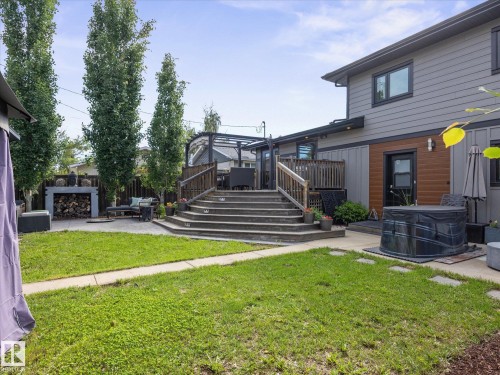 Spacious backyard featuring a multi-level wooden deck with stairs, a concrete patio area, and a lush green lawn - 8822 161 Street, Edmonton, AB 