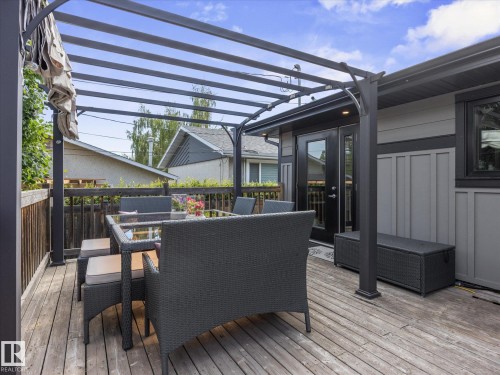 Spacious outdoor deck featuring a dark metal pergola, wood-finish flooring, and a dark wood railing - 8822 161 Street, Edmonton, AB 