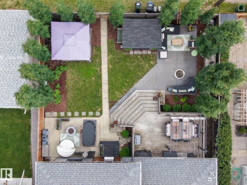 Expansive backyard featuring a multi-level deck with an integrated pergola, a spacious patio area with a fire pit, mature perimeter trees, and manicured lawn sections - 8822 161 Street, Edmonton, AB 