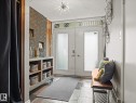 Entryway featuring double doors with frosted glass, wood-finish flooring, a contemporary ceiling light fixture, a built-in brick feature wall with display niches, and a built-in wood-finish shelving unit - 8822 161 Street, Edmonton, AB 