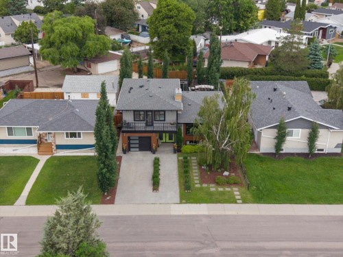 Contemporary exterior featuring a flat roofline, dark siding, an integrated garage, a second-story balcony, and a well-maintained front yard with mature landscaping and a stepping stone pathway - 8822 161 Street, Edmonton, AB 