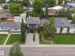 Contemporary exterior featuring a flat roofline, dark siding, an integrated garage, a second-story balcony, and a well-maintained front yard with mature landscaping and a stepping stone pathway - 