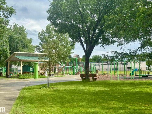 Green park setting featuring a shaded structure, multiple play equipment areas, mature trees, and a concrete pathway - 8822 161 Street, Edmonton, AB 