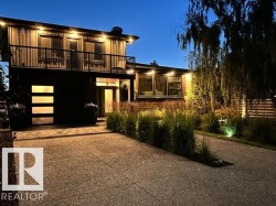 Modern architectural exterior featuring a second-story balcony with dark railing, an integrated garage door with horizontal frosted glass panels, and a concrete driveway - 