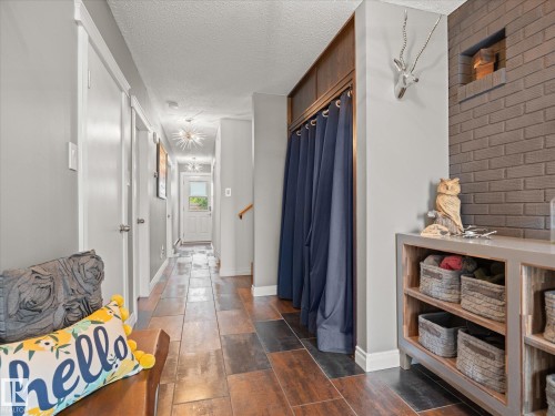 Hallway featuring multi-toned wood-finish flooring, a built-in storage unit with open shelving, a brick-textured accent wall, and a built-in closet with curtain enclosure - 8822 161 Street, Edmonton, AB 