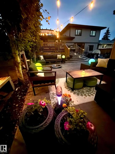 Expansive multi-level paved patio area featuring string lighting, built-in deck lighting, a wood deck with railings, and established landscaping - 8822 161 Street, Edmonton, AB 