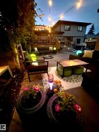 Expansive multi-level paved patio area featuring string lighting, built-in deck lighting, a wood deck with railings, and established landscaping - 
