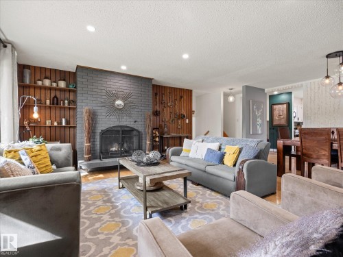 Living area featuring a gray brick fireplace with a hearth, recessed lighting, and wood-finish wall paneling with built-in shelving - 8822 161 Street, Edmonton, AB 