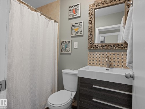 Bathroom featuring a wood-finish vanity with an integrated basin sink, a tiled backsplash, and a decorative framed mirror - 8822 161 Street, Edmonton, AB 