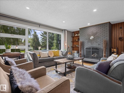 Living area featuring a gray brick fireplace with an arched firebox, wood paneling, built-in shelving, recessed lighting, and large picture windows - 8822 161 Street, Edmonton, AB 