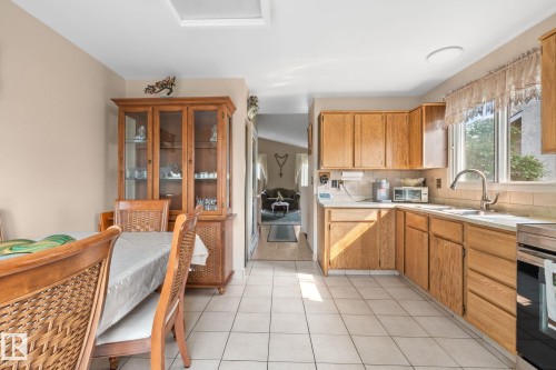 Kitchen featuring wood cabinetry, white tile flooring, white countertops, and a stainless steel oven - 18126 98 Avenue, Edmonton, AB 