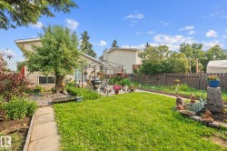 Spacious backyard featuring a manicured lawn, concrete patio area with pergola, and mature trees - 