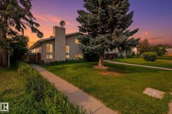 Exterior siding residence featuring multiple windows, a prominent chimney, and mature trees on a grassy lawn with a concrete pathway - 