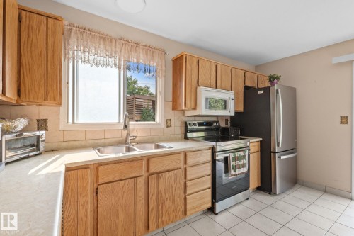 Kitchen featuring wood cabinetry, a double basin stainless steel sink, tile countertops, and a tile backsplash - 18126 98 Avenue, Edmonton, AB 