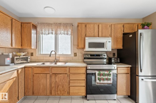 Kitchen featuring wood cabinetry, white tile flooring, light countertops, a double basin sink with a gooseneck faucet, and a white oven with a built-in microwave - 18126 98 Avenue, Edmonton, AB 