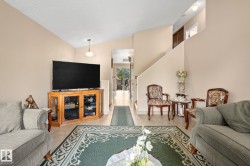Vaulted ceiling living area with neutral wall tones, tile flooring, and a staircase - 