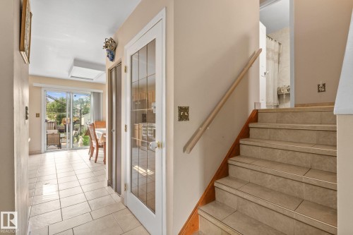 Tiled staircase with wood handrail, featuring light-toned tile flooring extending to the sliding glass door - 18126 98 Avenue, Edmonton, AB 