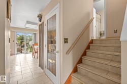 Tiled staircase with wood handrail, featuring light-toned tile flooring extending to the sliding glass door - 