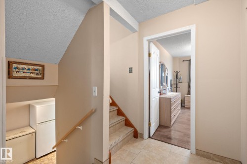 Tiled flooring entryway featuring a staircase with a wooden handrail and a doorway leading to a room with wood-finish flooring - 18126 98 Avenue, Edmonton, AB 