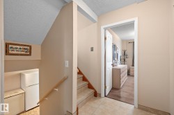 Tiled flooring entryway featuring a staircase with a wooden handrail and a doorway leading to a room with wood-finish flooring - 
