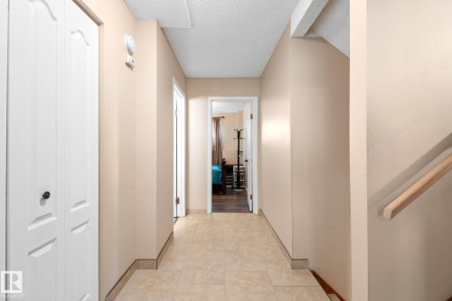 Hallway with neutral wall paint, tile flooring, white bi-fold closet doors, and a natural wood handrail - 18126 98 Avenue, Edmonton, AB 
