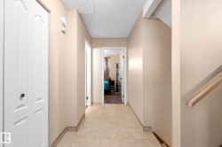 Hallway with neutral wall paint, tile flooring, white bi-fold closet doors, and a natural wood handrail - 