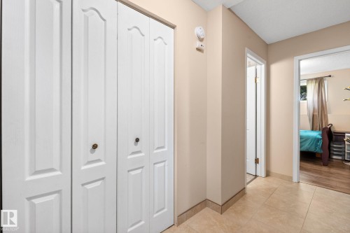 Hallway featuring light-toned tile flooring, neutral wall paint, and white paneled bifold doors with brass-finish knob hardware - 18126 98 Avenue, Edmonton, AB 