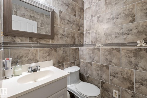 Bathroom featuring floor-to-ceiling rectangular wall tiles, a decorative glass tile border, a white vanity with an integrated sink, a chrome faucet, and a wall-mounted mirror - 18126 98 Avenue, Edmonton, AB 